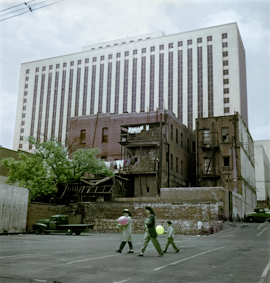 Altes Gebäude mit Balkonen und Wäscheleinen, dahinter ein neueres Hochhaus, vorne im Bild geht eine Familie mit Luftballonen 