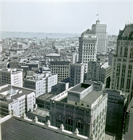 Blick Richtung Osten zur Bucht von San Francisco, am Horizont Schiffe, Montgomery Tower mit USA-Flagge, links im Bild das Flatiron Builing an der Ecke Market Street/Sutter Street, oben links Schienentrassee zum Bahnhof Third+Thousand Depot (gab es 1914-1976)