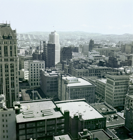 Blick Richtung Südosten, Montgomery Tower mit USA-Flagge, vorne Gebäude mit Dachfenstern an der Sutter Street, in der Bildmitte zwei Gebäude von San Francisco Chronicle, rechts Bank of Amerika und Gebäude mit Kuppel an der Market Street, im Hintergrund Hügel