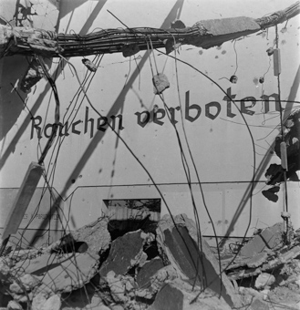 Wand mit Aufschrift «Rauchen verboten» und «Acces a parachutes», oben im Bild ein herabgestürzter Pfeiler mit Armierungseisen