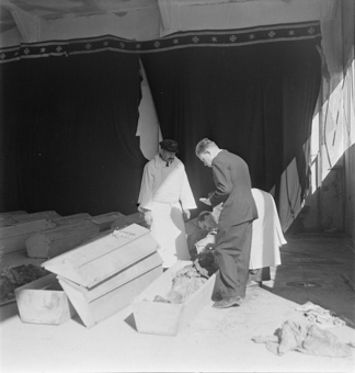 Zwei Bestatter in weissen Schürzen und ein Mann in Anzug beim Notieren/Dokumentieren