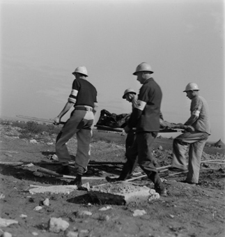 Vier Rotkreuzfreiwillige mit einem exhumierten Leichnam auf einer Tragebahre