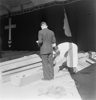 Zwei Bestatter in weissen Schürzen und ein Mann in Anzug beim Notieren/Dokumentieren