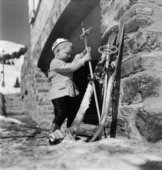 Kind stellt Skis und Stöcke an eine Hauswand