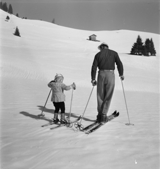 Kind und Skilehrer beim Aufstieg mit Skis und Stöcken