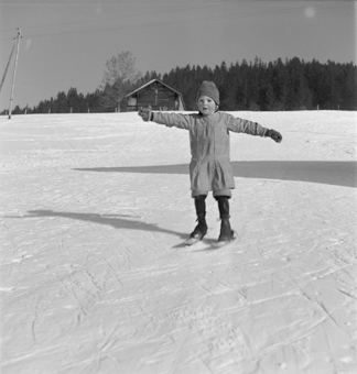 Kind fährt auf kurzen Skis (Fassdauben) einen Hang runter