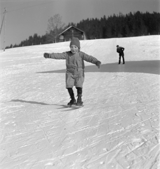 Kind fährt auf kurzen Skis (Fassdauben) einen Hang runter