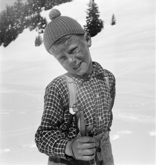 Knabe in kariertem Hemd mit Skistock an einem Schneehang