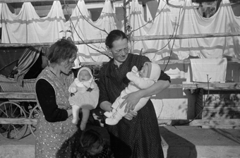 Zwei Frauen mit zwei Babys und einem Mädchen vor der Laube eines Bauernhauses