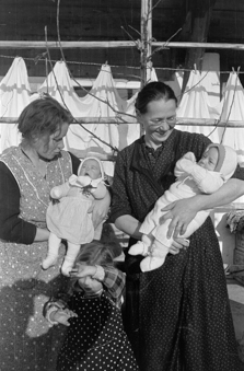 Zwei Frauen mit zwei Babys und einem Mädchen vor der Laube eines Bauernhauses