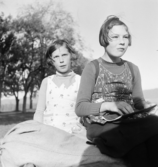Zwei Mädchen im Freien sitzend, mit Schulheft
