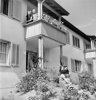 Einstöckige Reihenhäuser mit Bewohnern auf Balkon und im Garten
