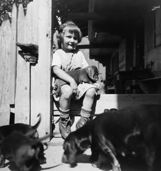 Sitzendes Mädchen mit jungen Hunden vor einem Bauernhaus