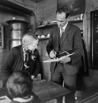 Lehrer mit Buch und Schiefertafel im Gespräch mit einer Schülerin 