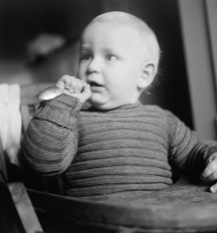 Kleinkind mit Löffel, in Kinderstuhl sitzend