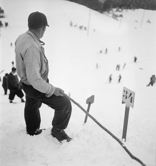 Mann am Pistenrand des Skispringens, Nummernschild als Markierung für Sprungweite