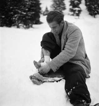 Im Schnee sitzender Mann am Bandagieren seines Fusses
