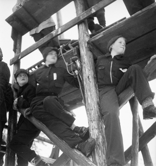 Zuschauer an Skispringen auf Gerüst eines Holzturms sitzend