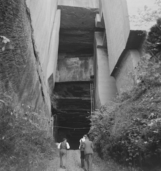 Drei Männer auf dem Weg ins Innere des Stockern-Steinbruchs, neben und vor ihnen hohe Sandsteinwände, eine Leiter und ein Seil mit Haken