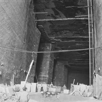 Steinbrecher bei der Arbeit mit Sandsteinblöcken, rechts eine Leiter, vorne ein Seil mit Haken zum Anheben von Lasten