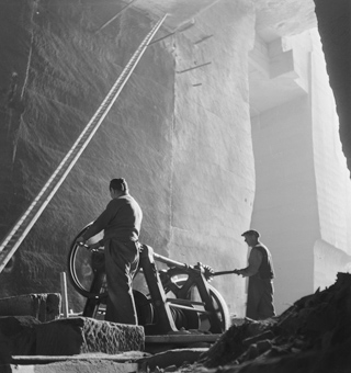 Zwei Arbeiter beim Brechen von Sandstein mit einem «Steinbrecher» (Zerkleinerungsmaschine) im Innern des Steinbruchs