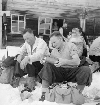 Zwei Männer beim Pic-Nic im Schnee vor einem Berghaus