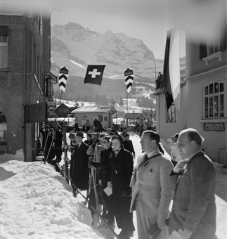Links im Bild Hotel Silberhorn, rechts Gebäude mit Sonnenterrasse und Coiffeur (Coiffeurs Bischoff), dazwischen Ski-Park und Fahnen vom Ski-Club Wengen