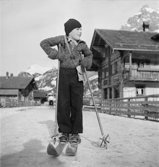 Knabe mit Skis auf einer Dorfstrasse