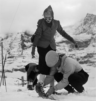 Mann ist einer Dame beim Anschnallen der Skis behilflich 