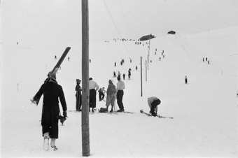Schneehang mit Skifahrern beim Aufstieg entlang von Telefonmasten