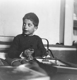 Knabe im Bett sitzend, Schachtel mit Spielzeugfiguren